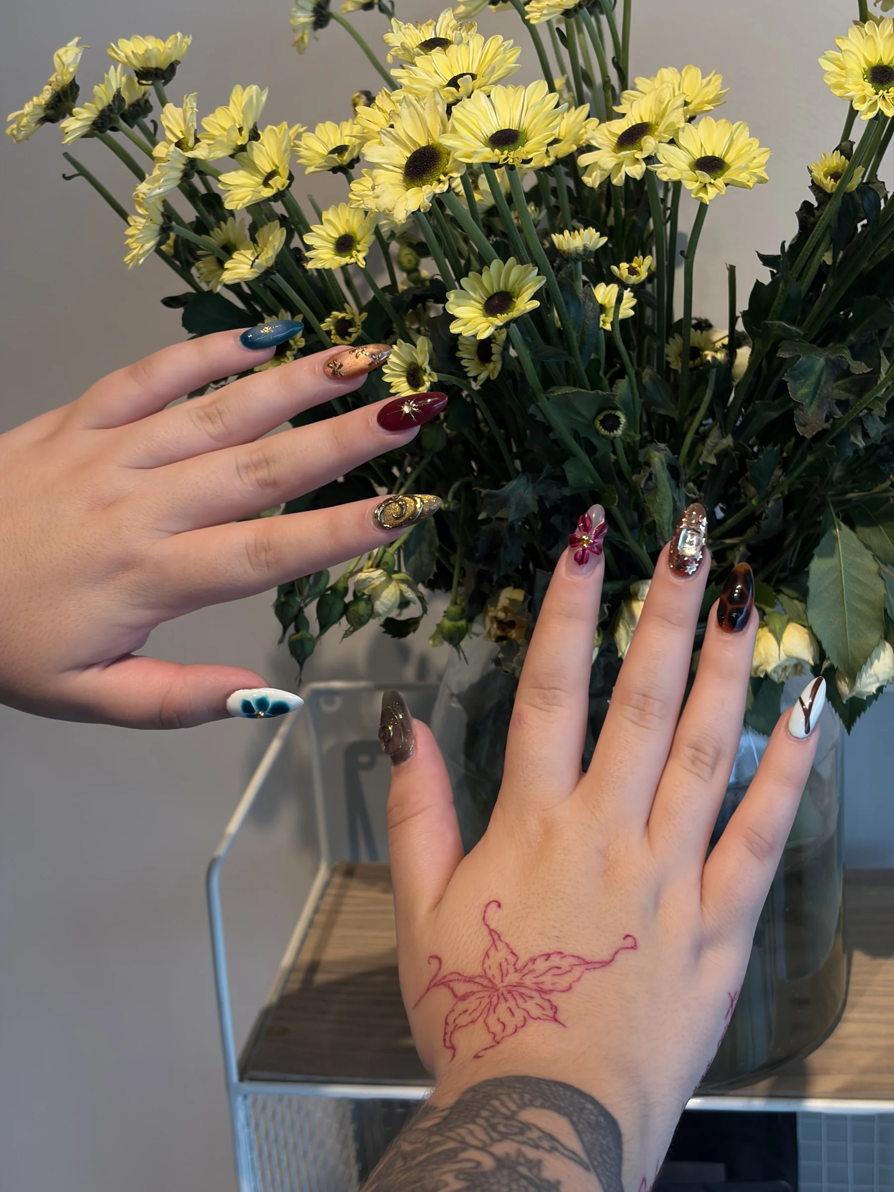 Un diseño distinto en cada uña junto a un ramo de flores amarillas
